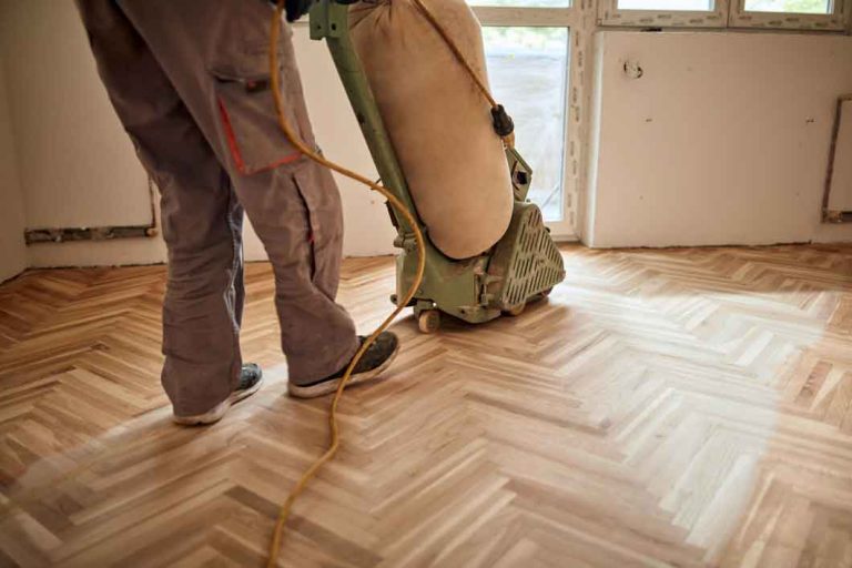 Repairman restoring parquet with a sanding machine.