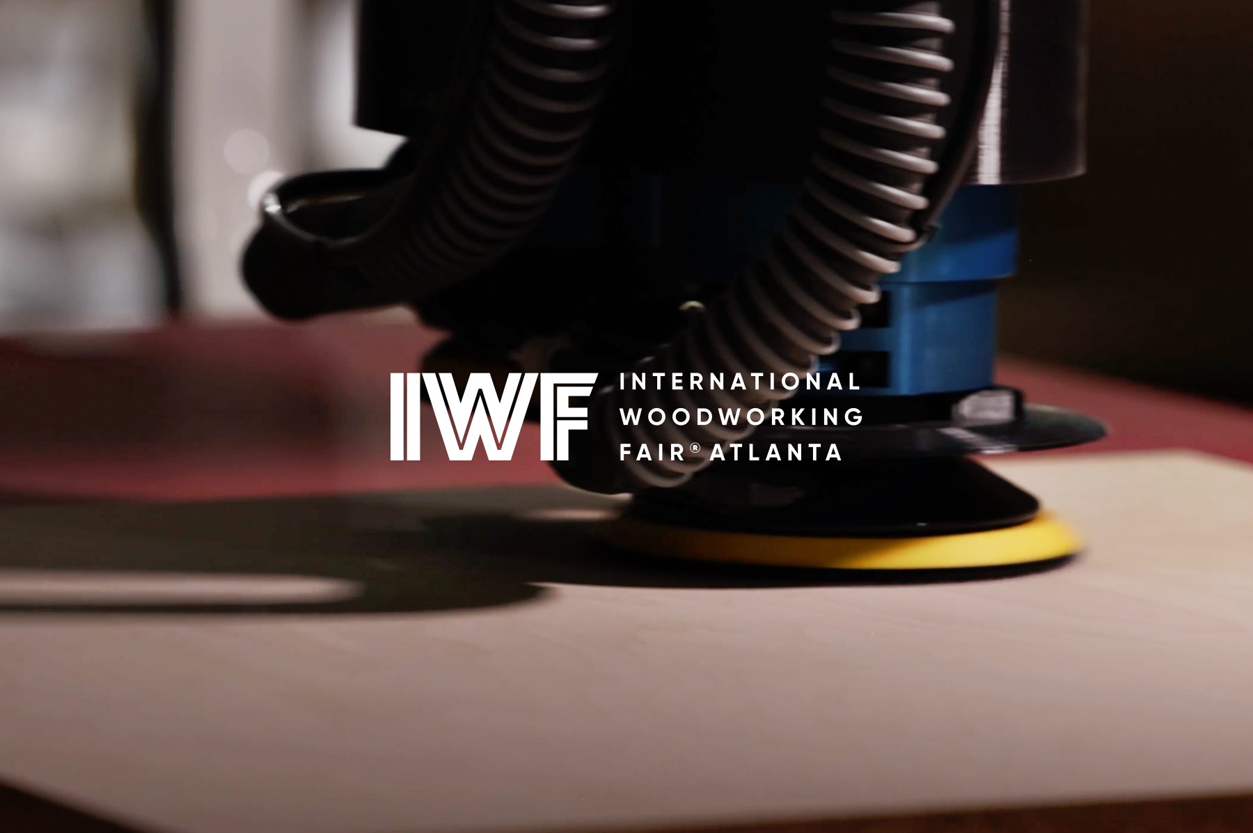 Close-up of a polishing tool on a wooden surface with the IWFF International Woodworking Fair Atlanta logo overlaid