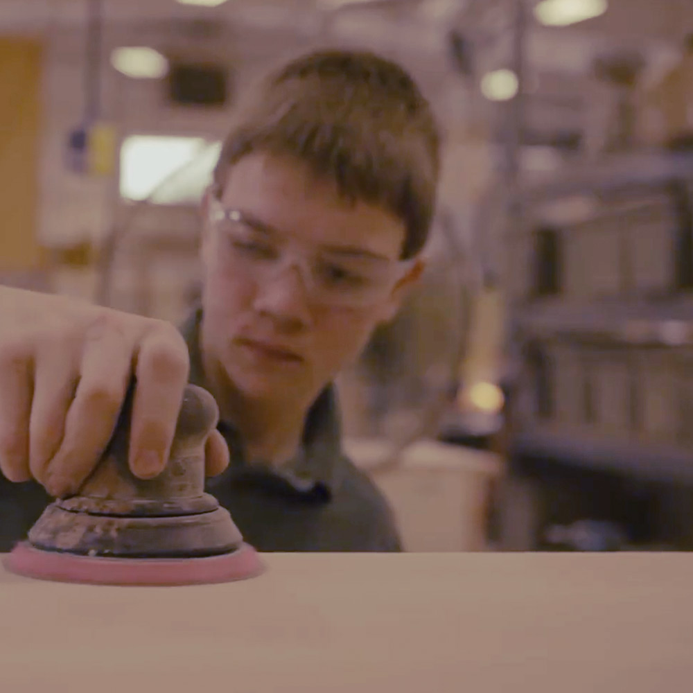 Person wearing safety glasses polishing a surface with a handheld grinder in a workshop.