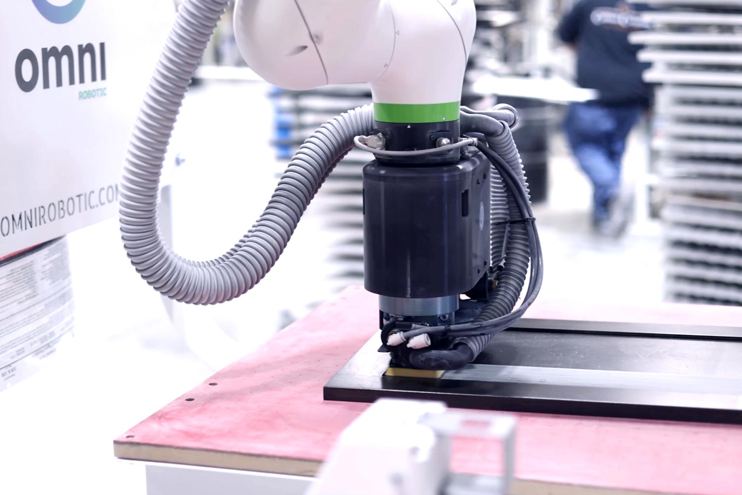 Close-up of a robotic arm with gray hoses mounted on a pink worktable in a factory setting.